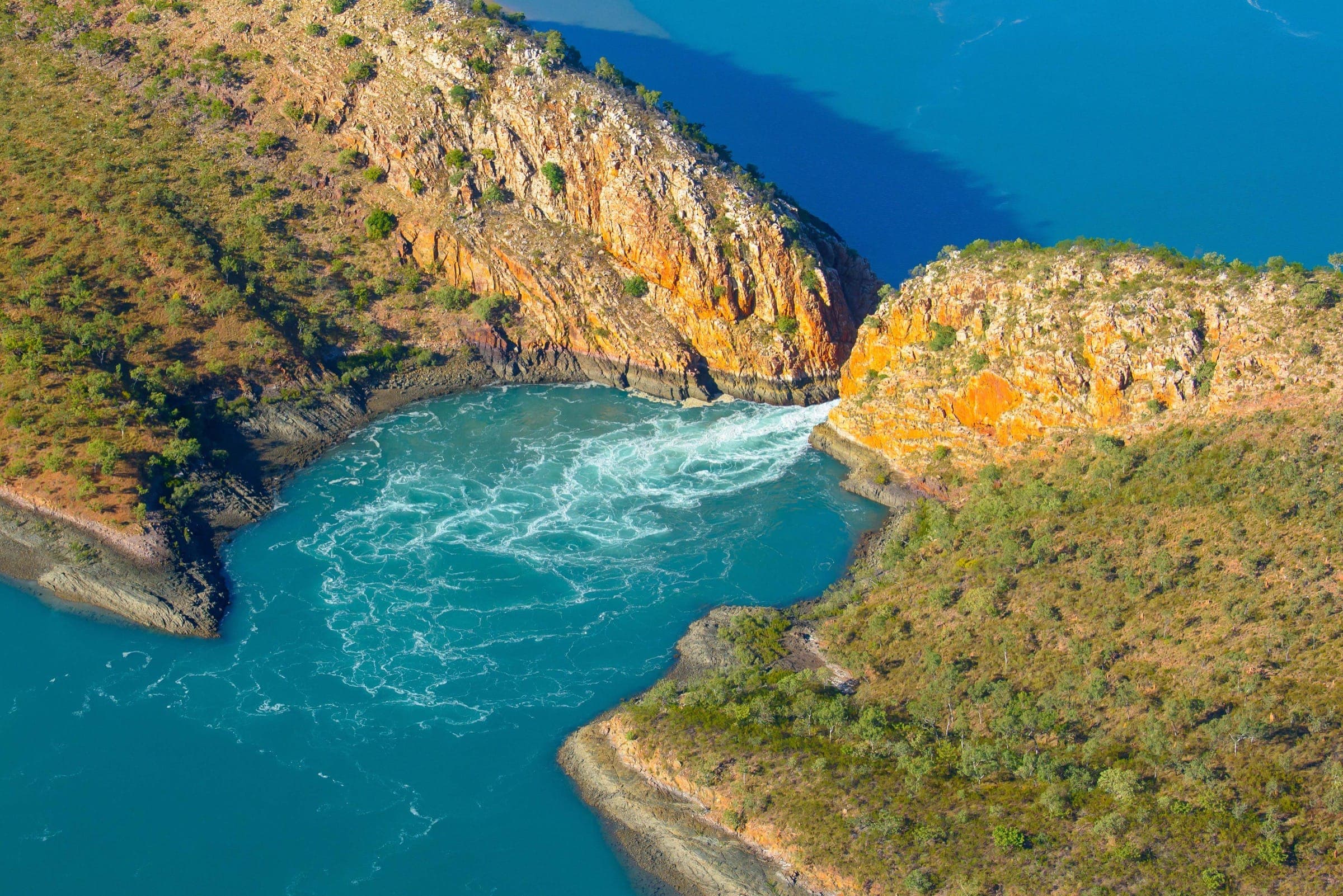 Two land masses almost touching above water, letting a stream of azure sea flow into a small blue-green bay